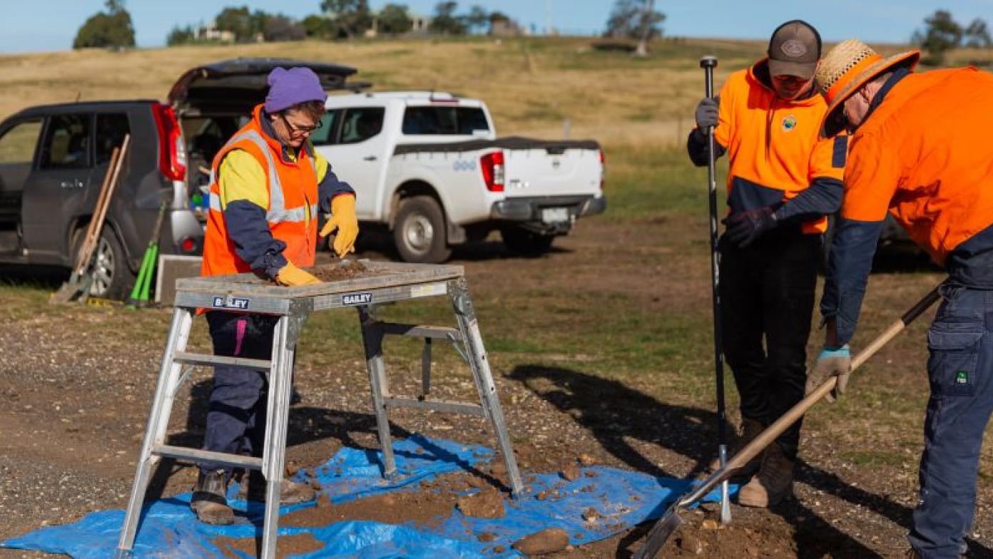 Three people sift rake soil.