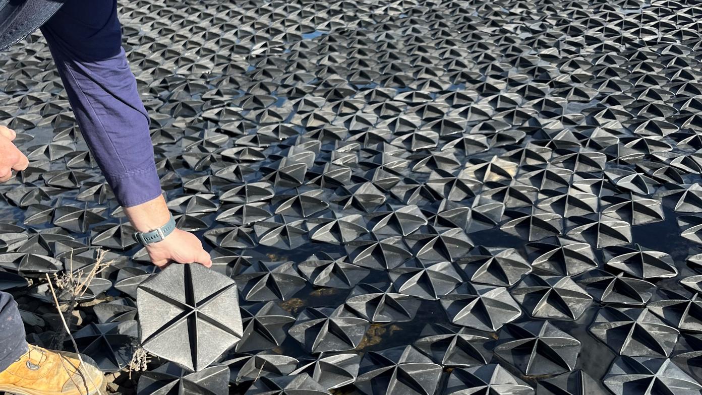 Man holds up a hexa-cover. Behind him the hexa-covers float on top of a body of water.