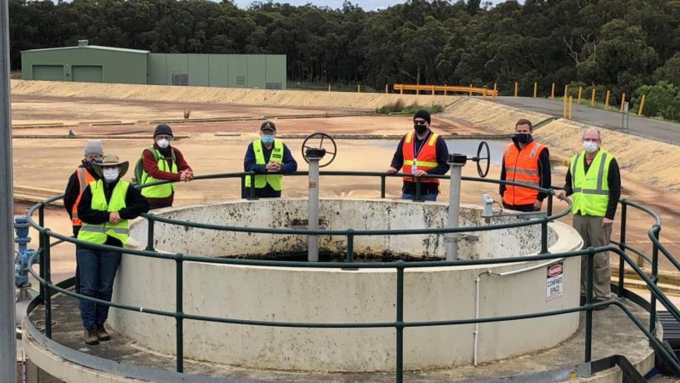 Men in hi-visibility vests stand around water basin. 