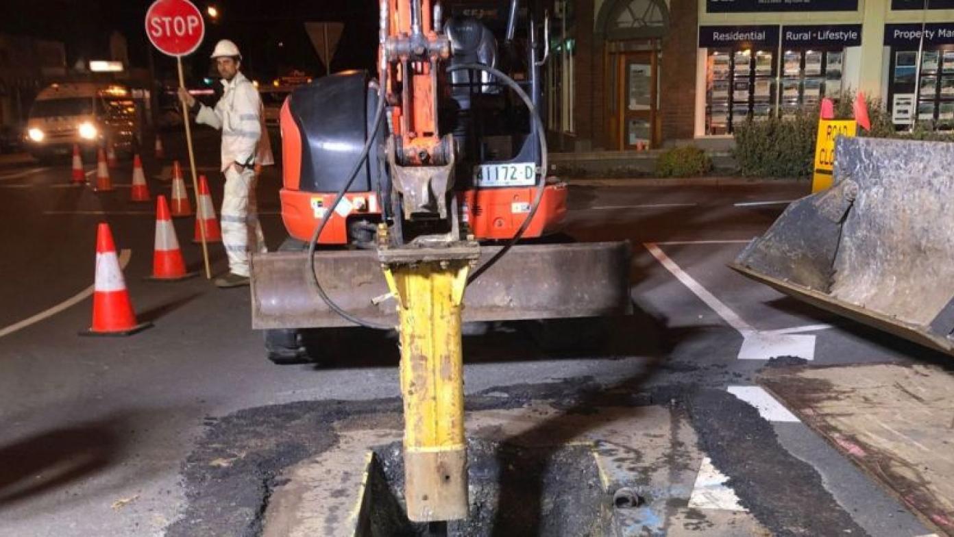 Street works, man holds stop sign on the left with machinery in centre.