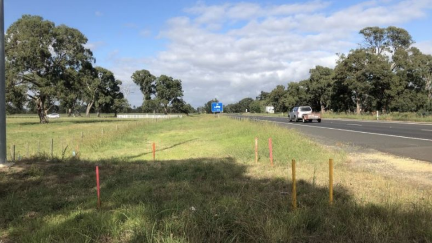 A grass area with a road on the right. A white utility drives down the road. 