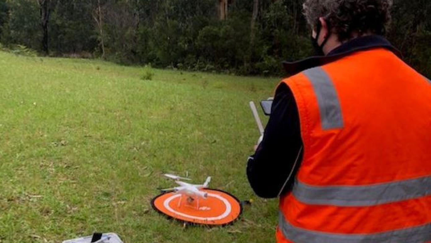 Person stands in right corner with drone in the centre. The man holds a remote. 