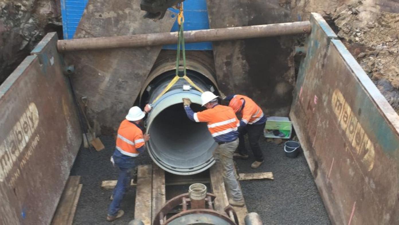 Three men hold end of a large pipe.