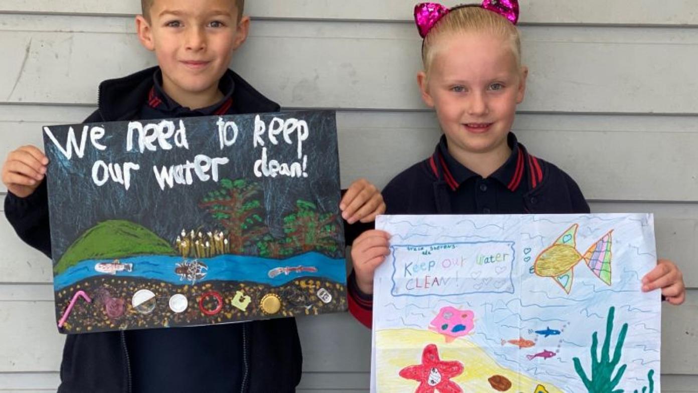 A boy and girl hold paintings depicting water and wildlife.