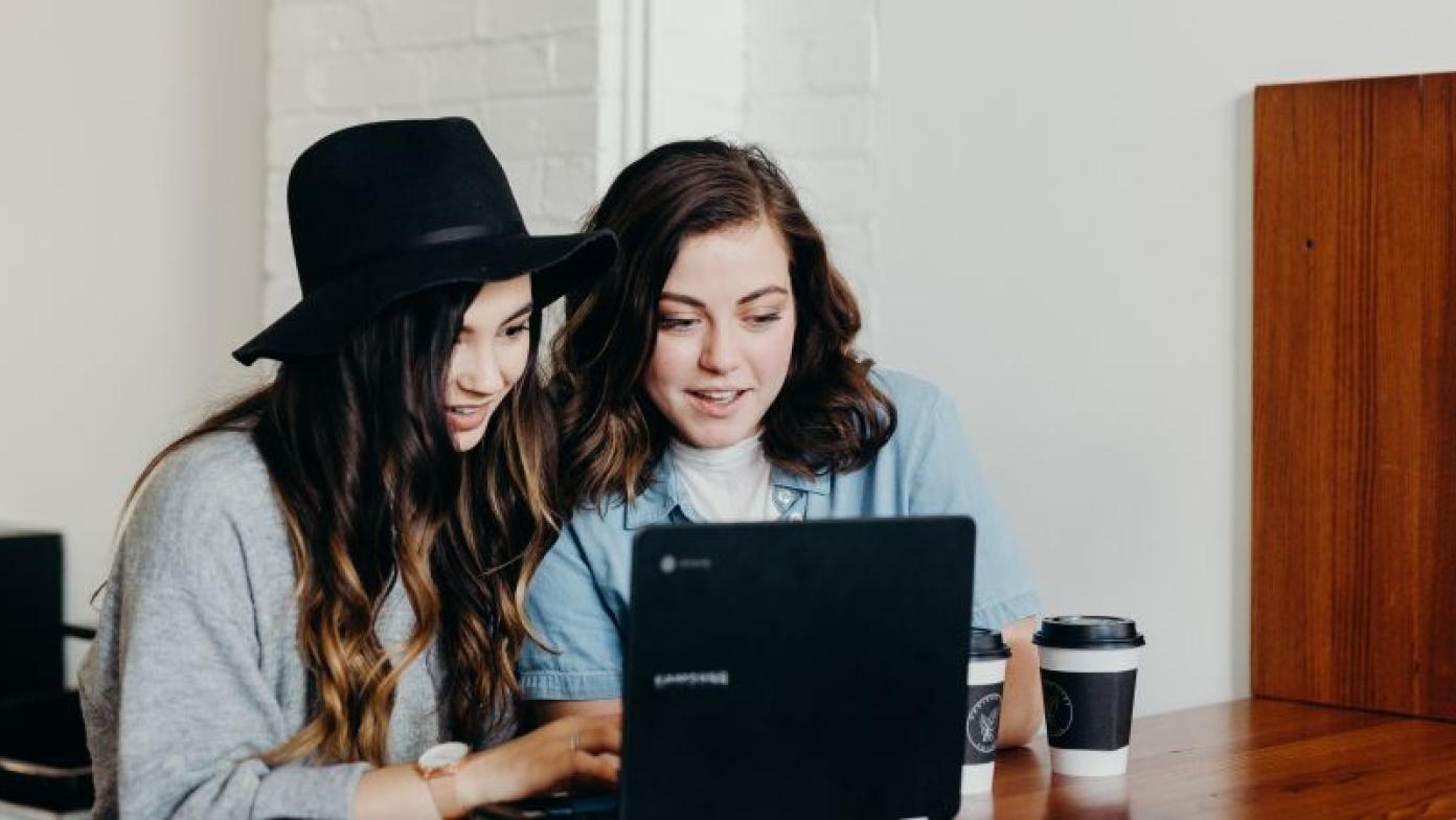 Two girls look at computer. 