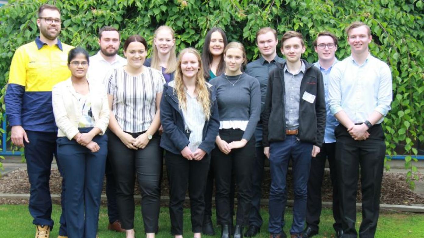 Students stand together in front of a tree in a garden. 