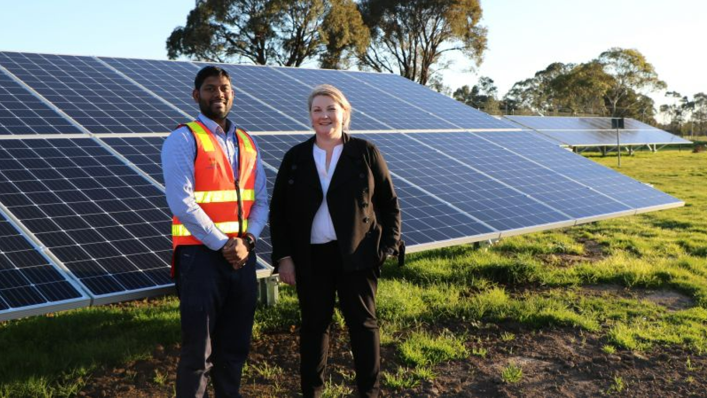 Man and woman stand in front of solar panels.