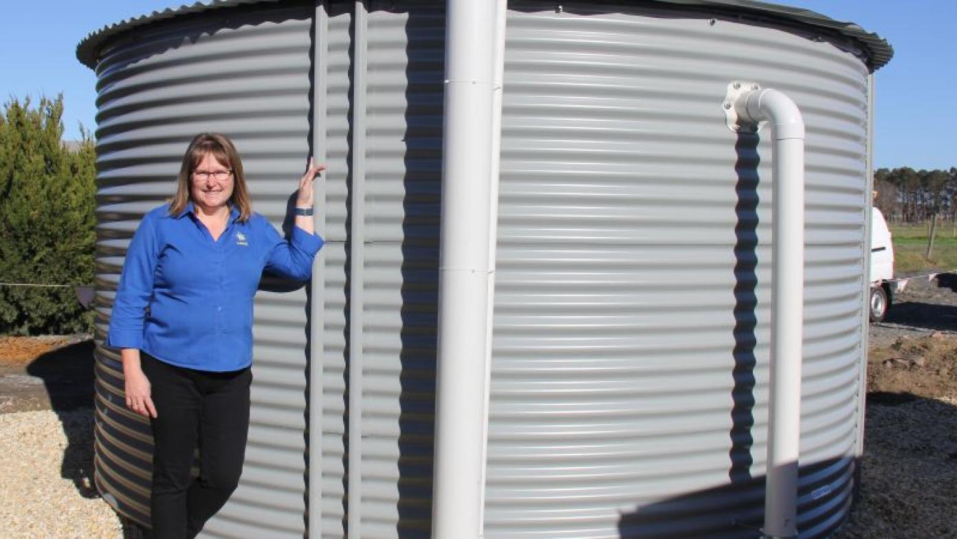 Woman stands next to grey water tank. 