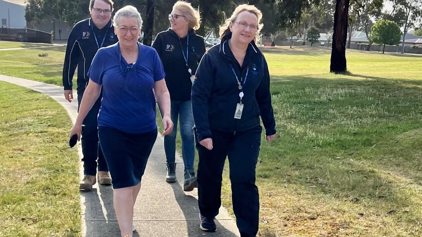 Four people in Gippsland Water uniform walk on a concrete path through a grass area