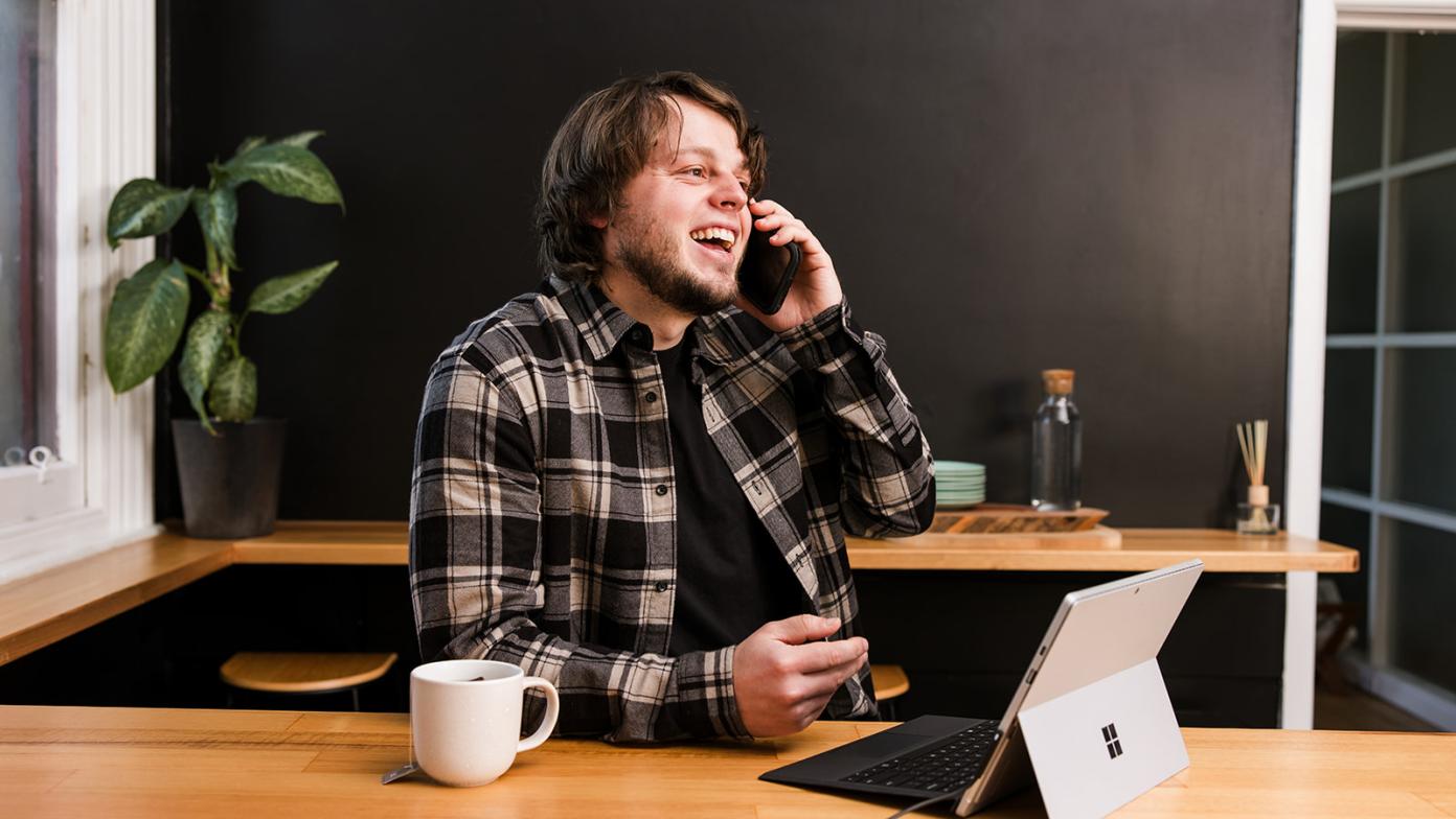 Man sits at bench talking on phone with computer in front of him.