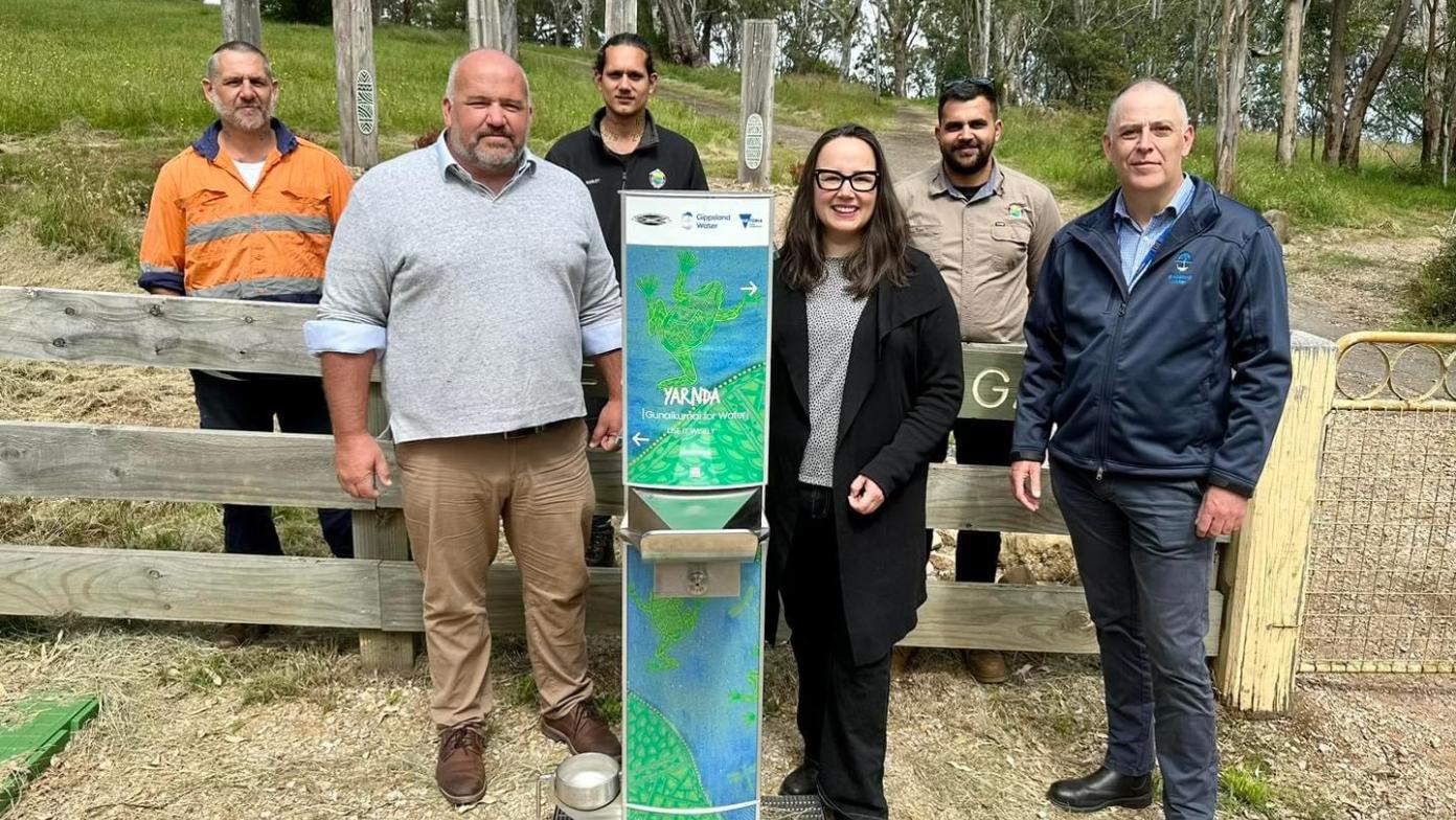 People stand around a water fountain in front of bushland