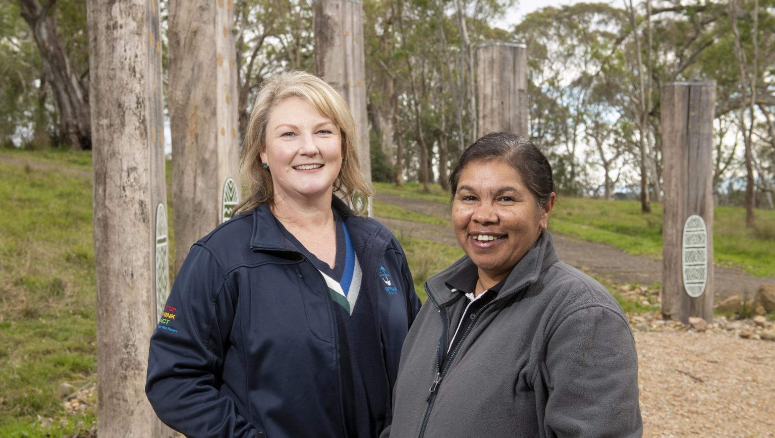 Sarah Cumming and Cath Thomas stand side by side in Knob Reserve. Trees are behind them.