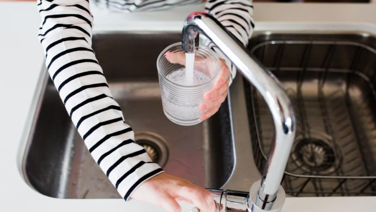 Woman fills up a glass of water over a stainless steel sink.