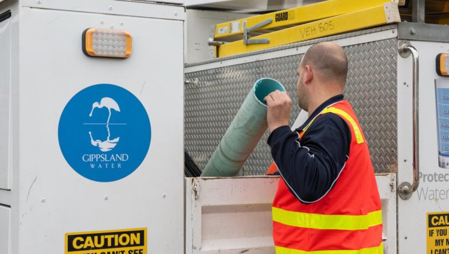 Man puts a pipe into the tray of a Gippsland Water utility vehicle. 