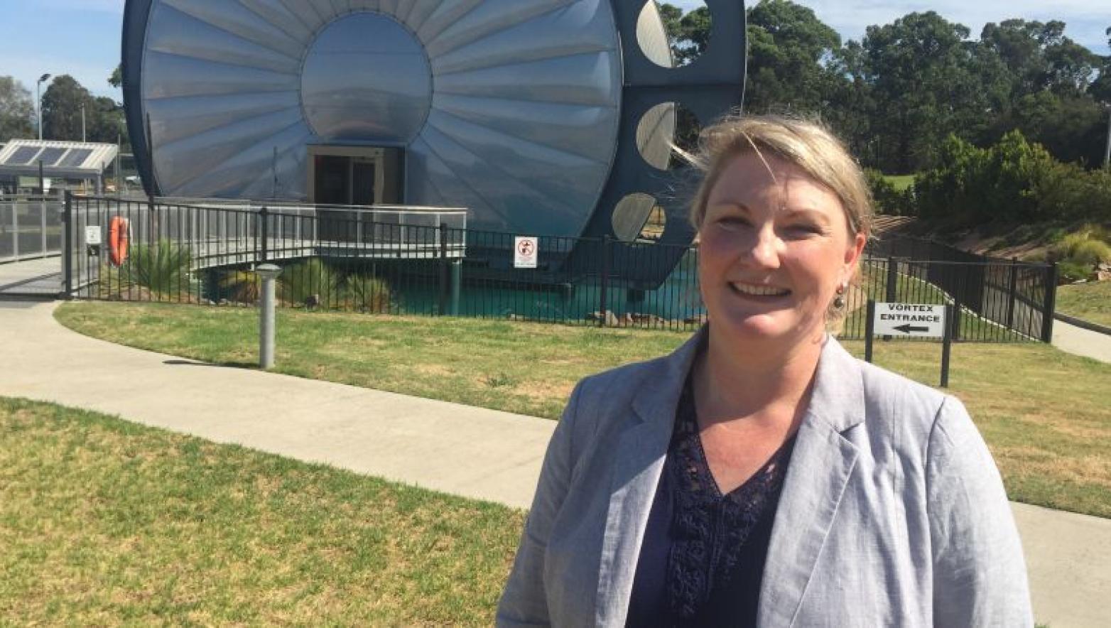 Sarah Cumming stands in front of large piece of machinery.