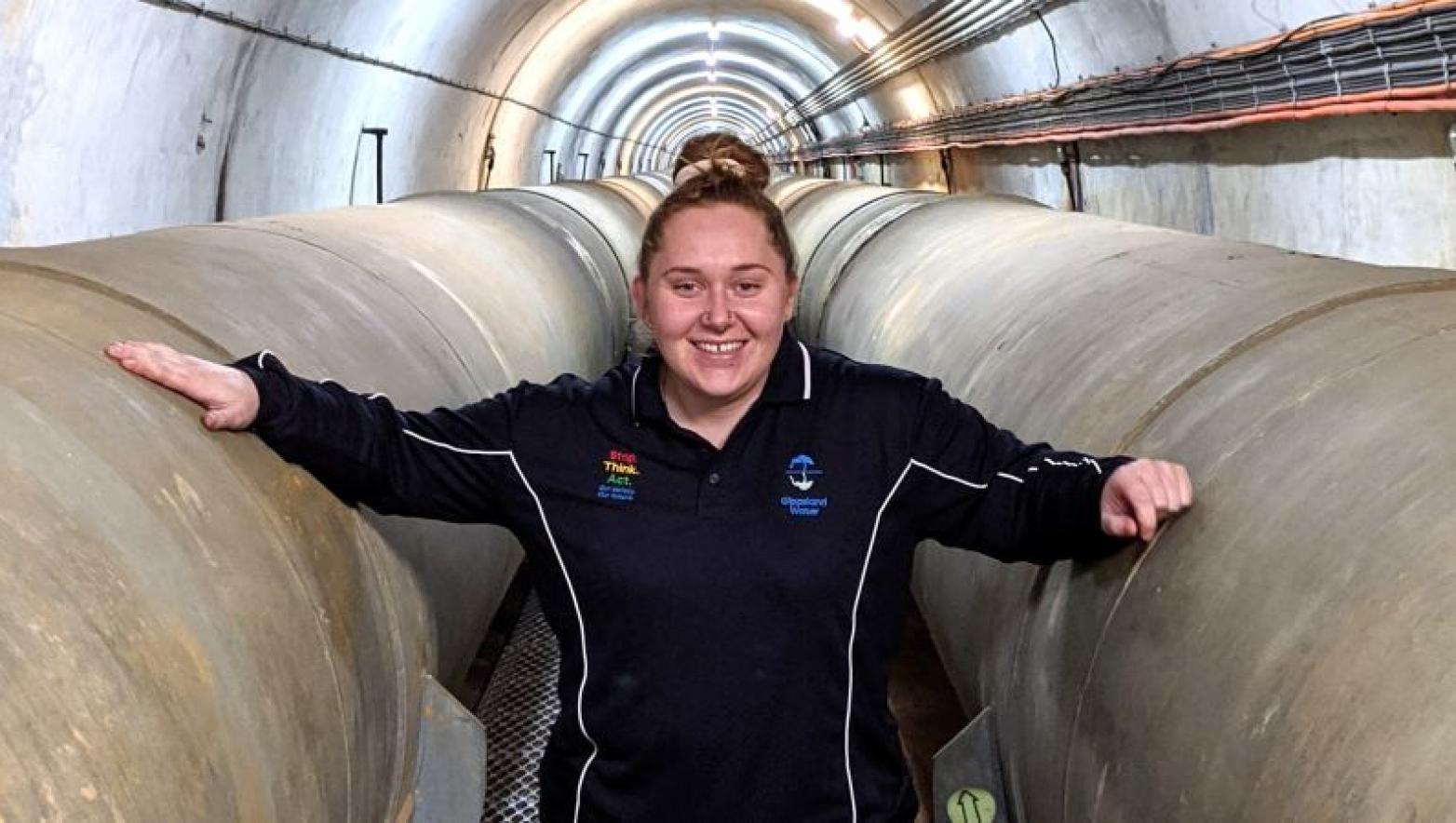 Young girl stands between pipes in Gippsland Water uniform.