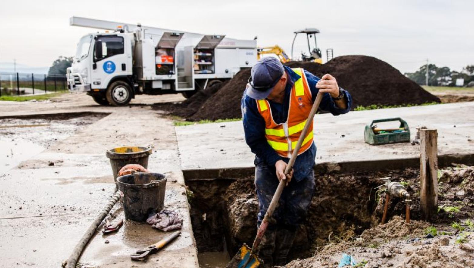 Man up to his knees in dirt digs a hole with shovel. He is in Gippsland Water uniform.