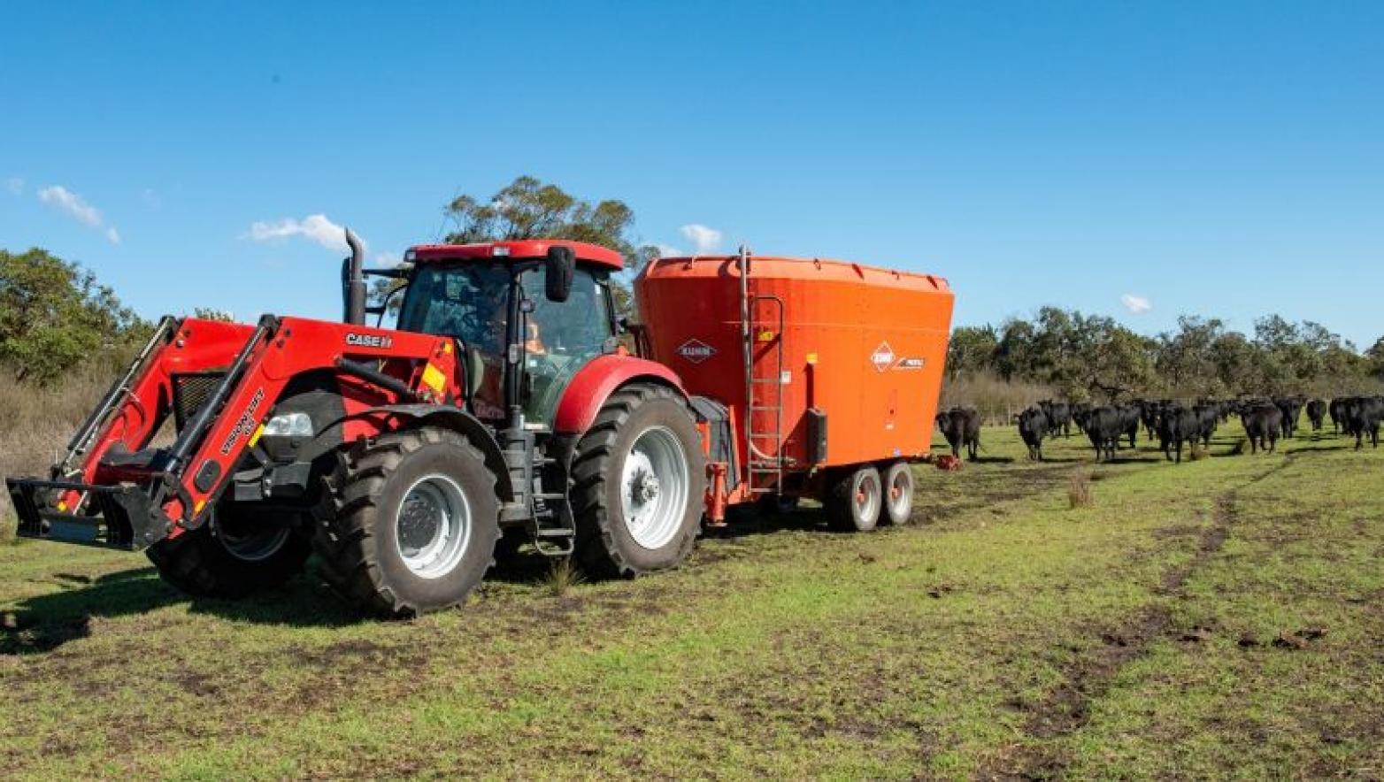 Tractor pulls orange trailer in paddock