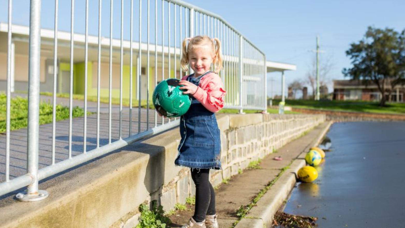 Young girl stands in street with soccer ball.