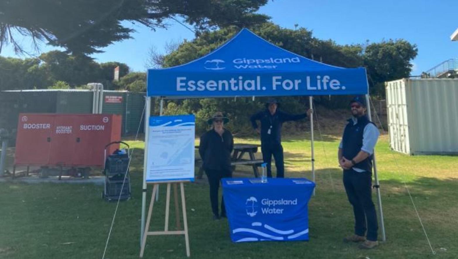 Three people stand under blue marquee