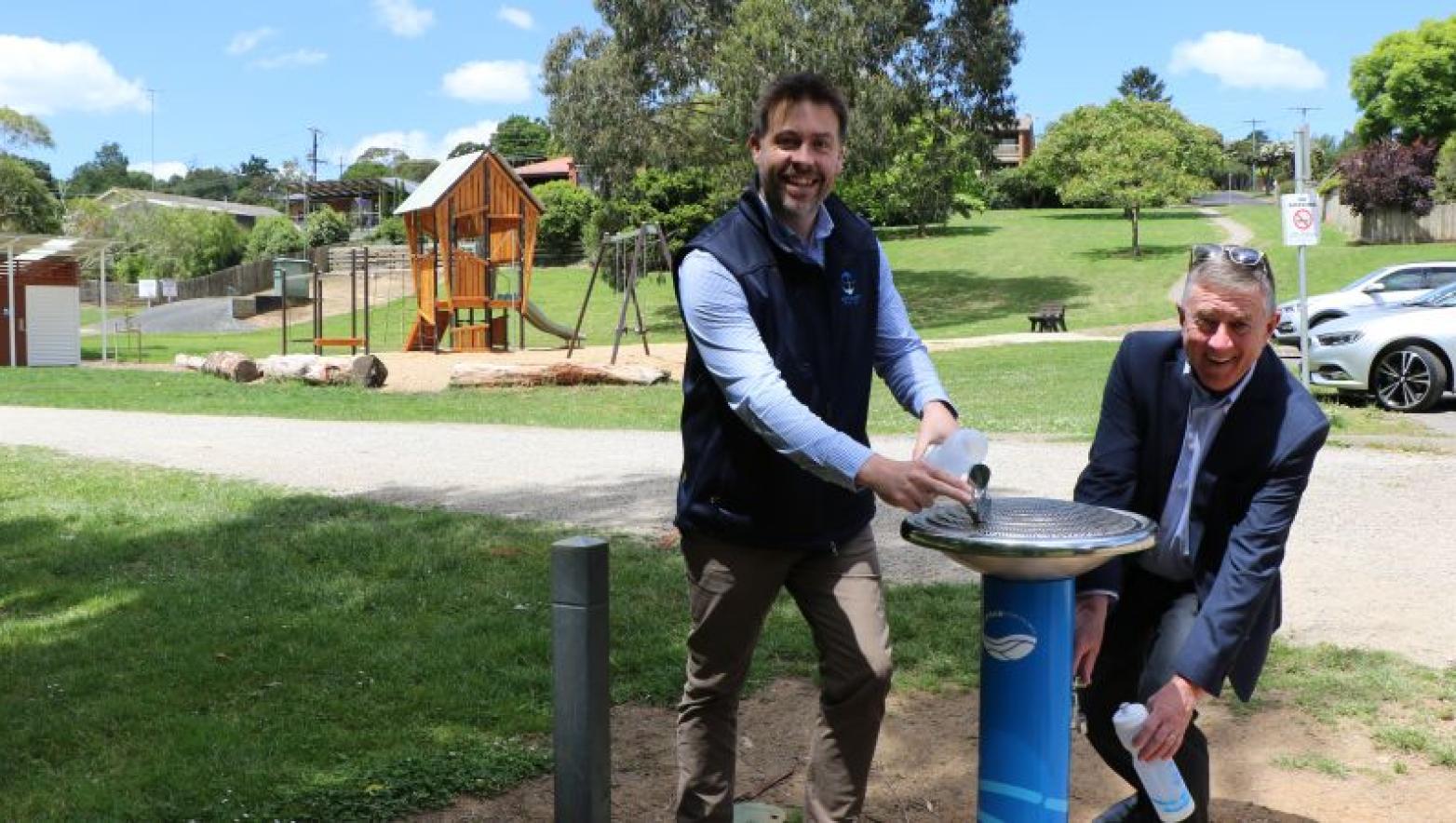 Two men stand on either side of a blue Gippsland Water drinking fountain. 