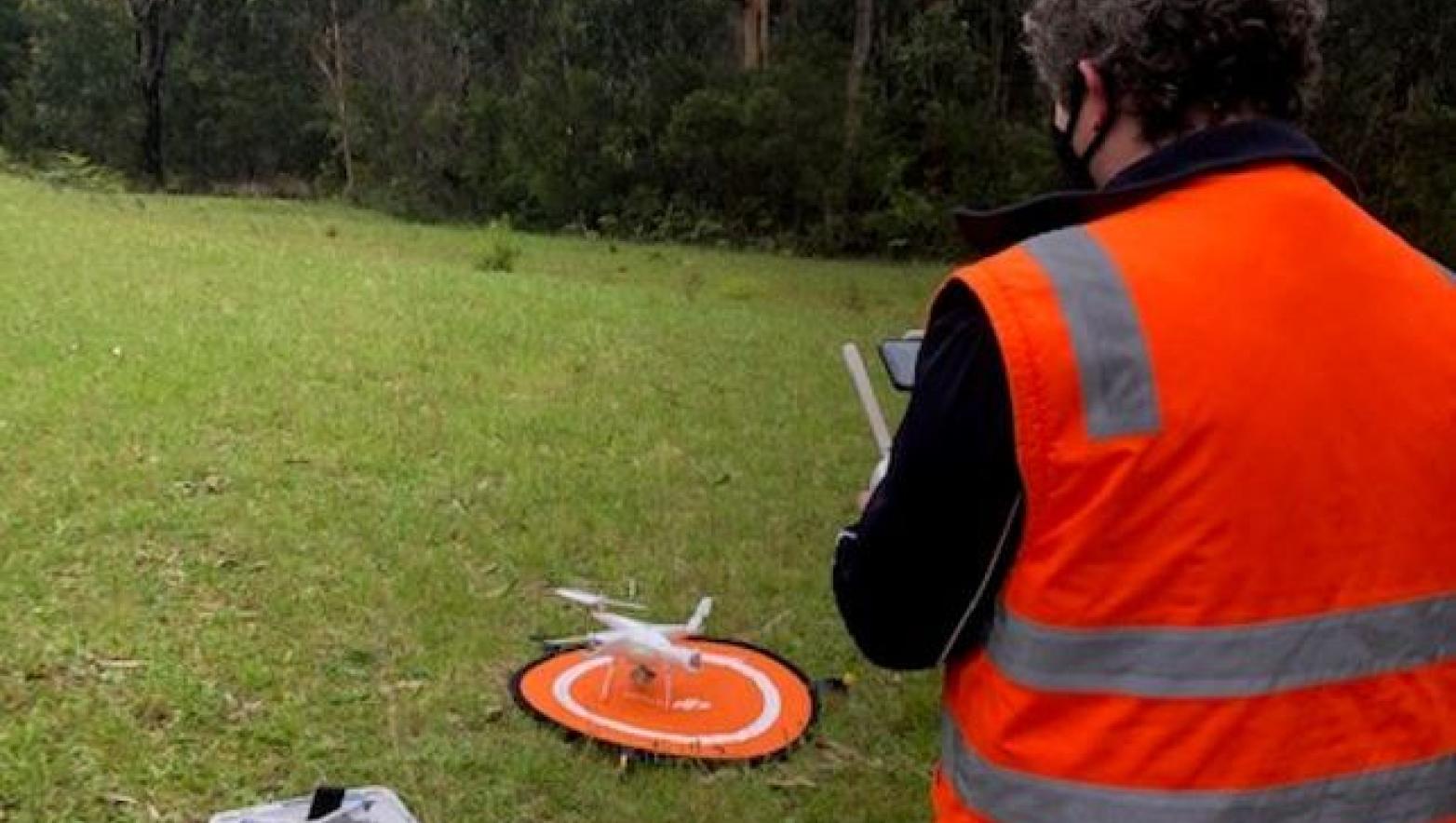 Person stands in right corner with drone in the centre. The man holds a remote. 