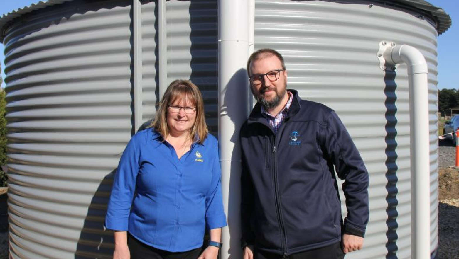 Two people in Gippsland Water uniform stand next to water tank.