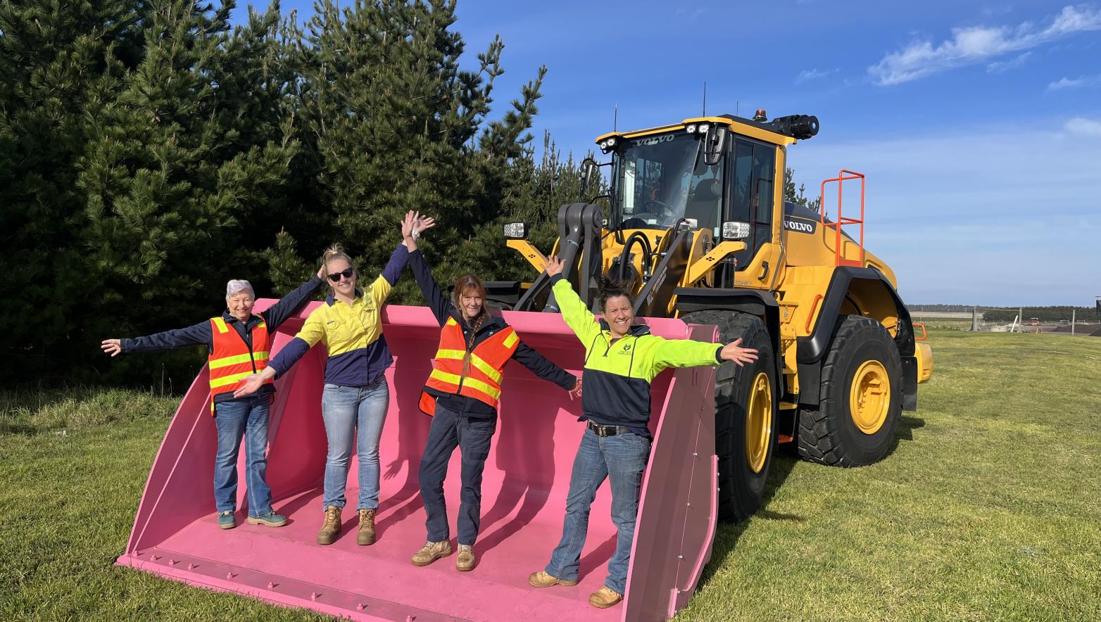 Three people stand in a pink bucket with their arms in the air. 