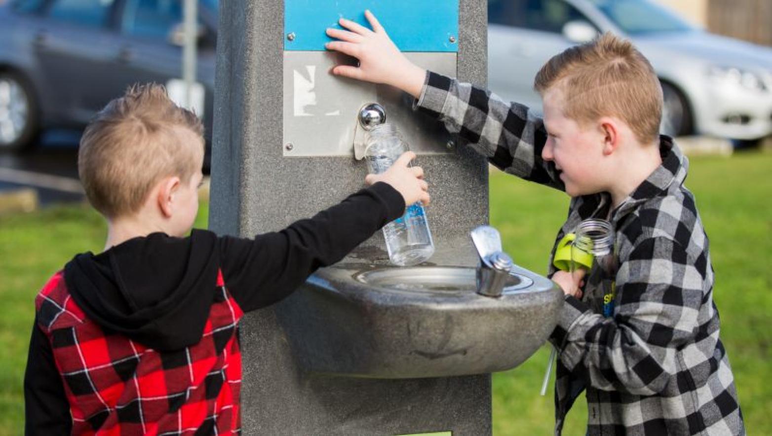 Two boys filled up drink bottles at water fountain.