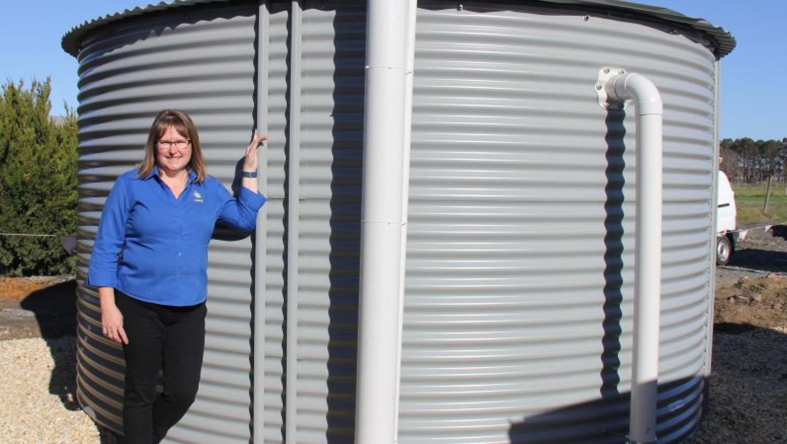 Woman stands next to grey water tank. 