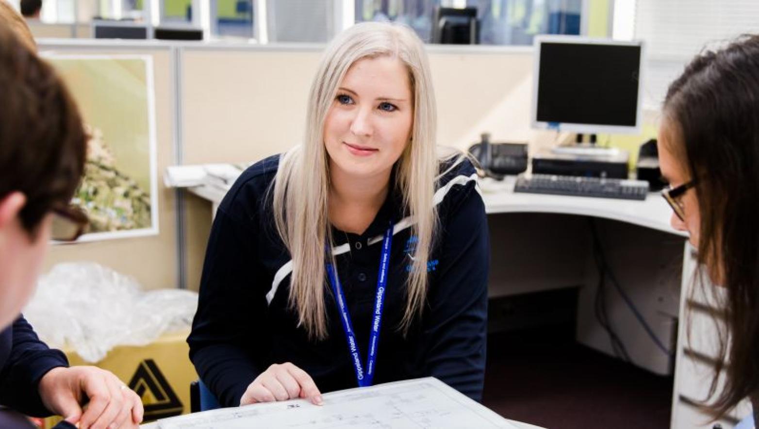 Woman in Gippsland Water unform sits at table with two other people. 