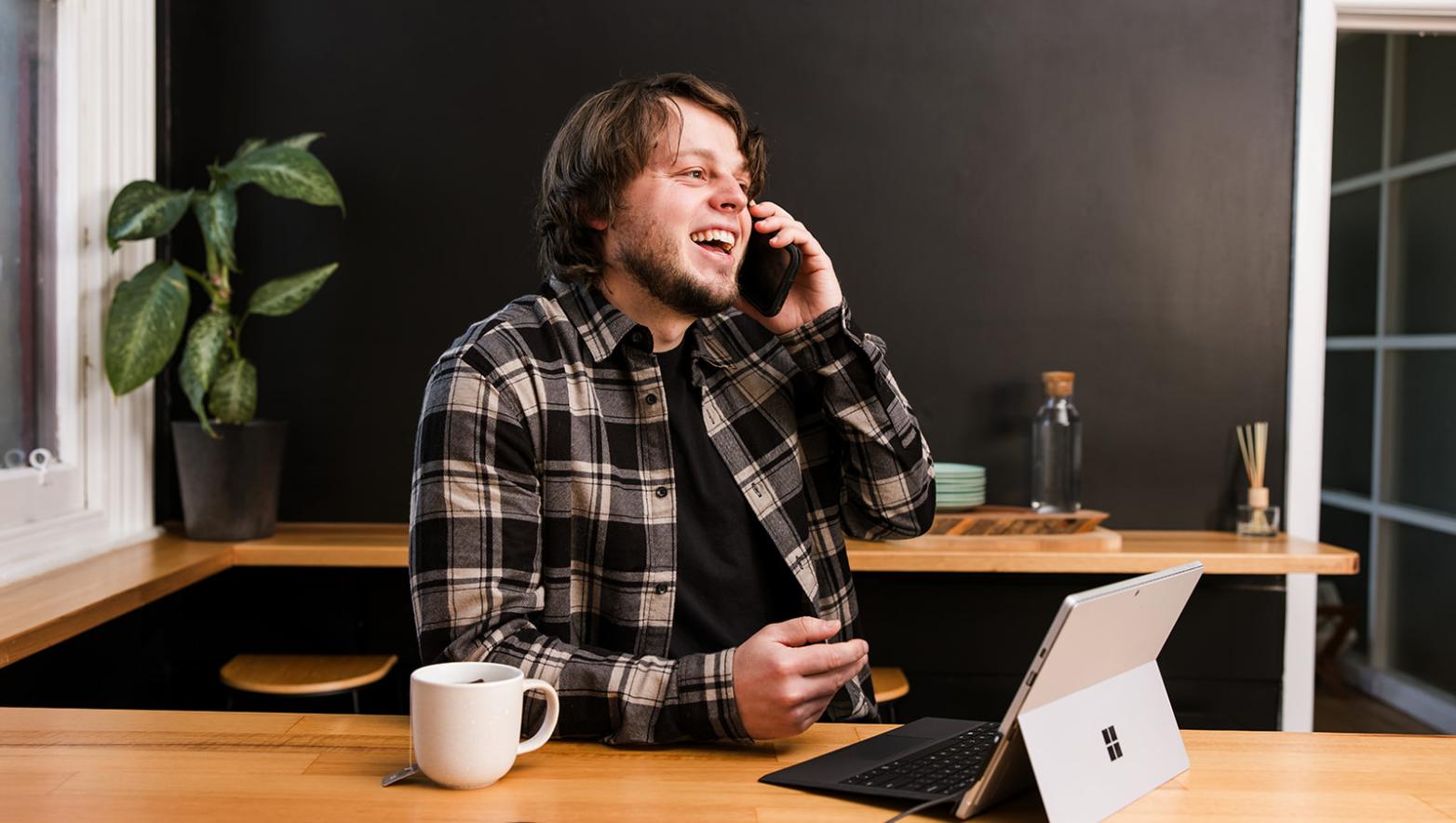 Man sits at bench talking on phone with computer in front of him.