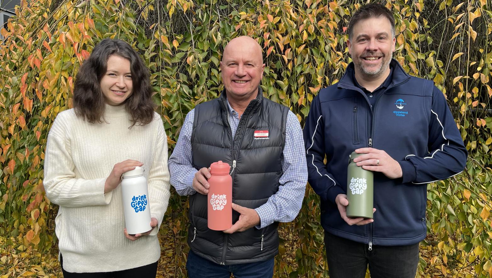 Jess, Nigel and Michael smiling and looking at the camera holding Drink Gippy Tap premium charity water bottles. 