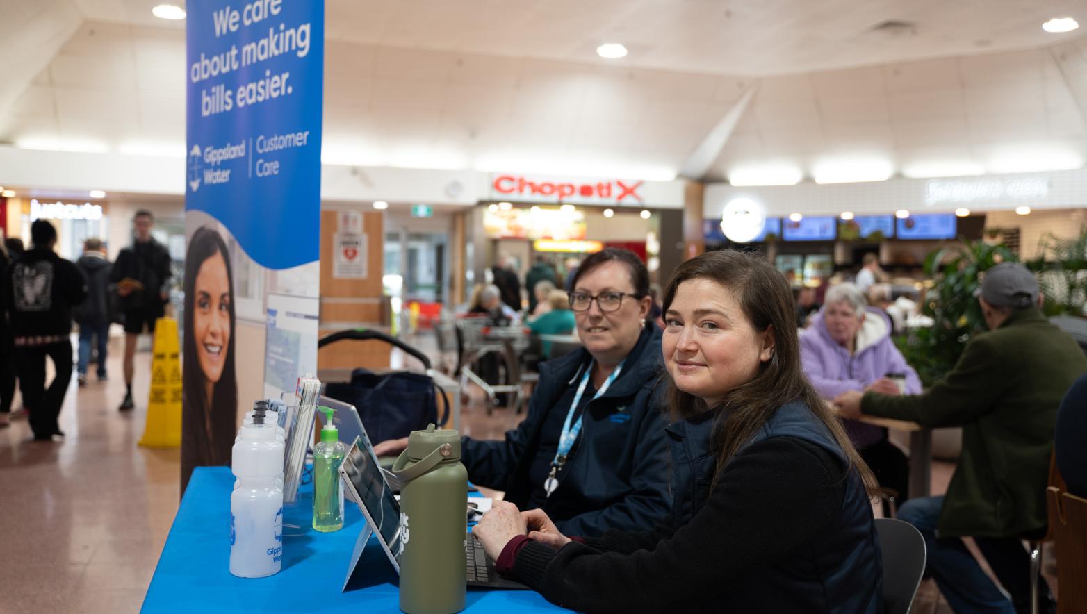 two people in gippsland water uniform sit in a shopping complex