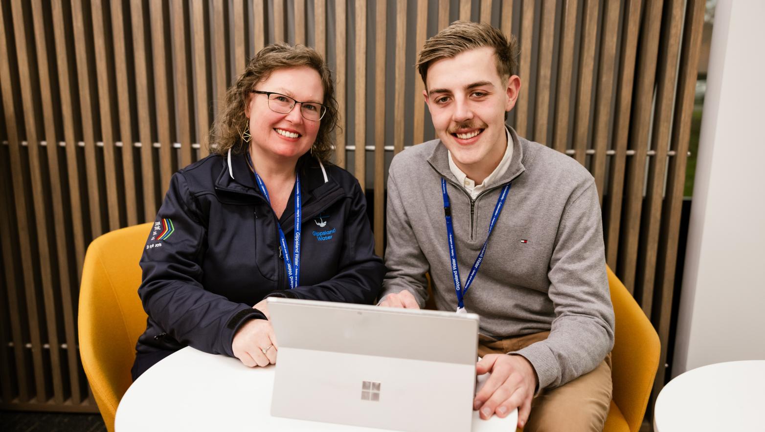 Two people sit behind laptop smiling