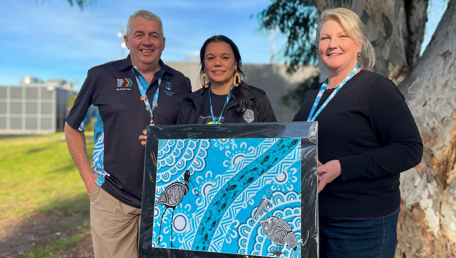 Three people hold a painting