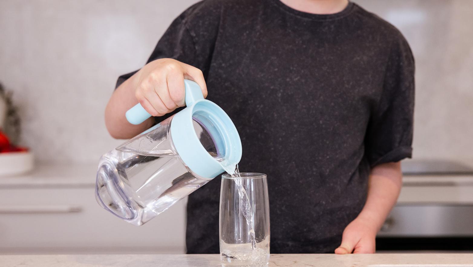 Person fills up a glass of water with a jug. 